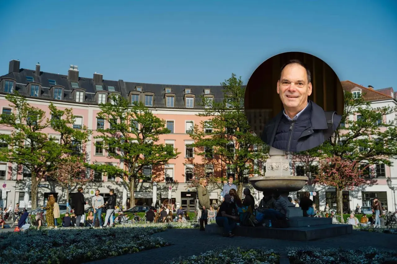 Ein Mann lächelt vor einem Brunnen und rosa Gebäuden im Glockenbachviertel München.