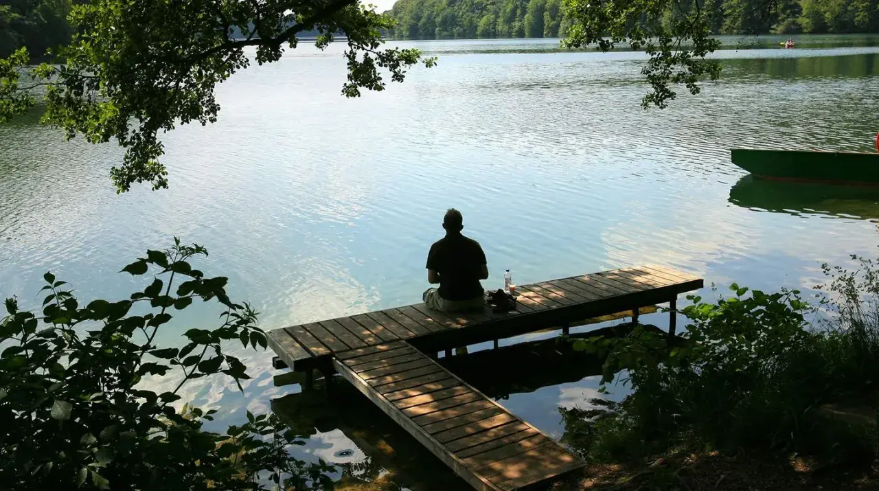 Mann sitzt auf Steg am See. Ein perfekter Ort, wo kann man in Deutschland Urlaub machen.