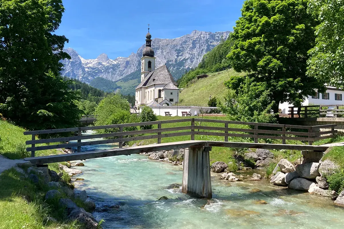 Idyllische Kirche mit Bergkulisse und Fluss – ein malerisches Motiv, das zu den beliebten Reisezielen Deutschlands zählt.
