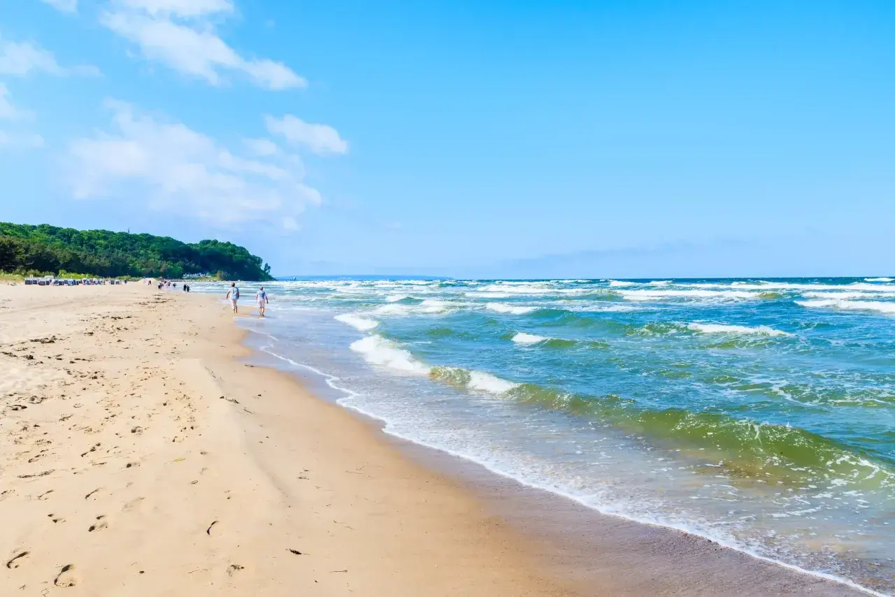 Ein sonniger Tag am Ostseebad Baabe. Menschen spazieren am breiten Sandstrand entlang, während die Wellen der Ostsee sanft ans Ufer rollen.