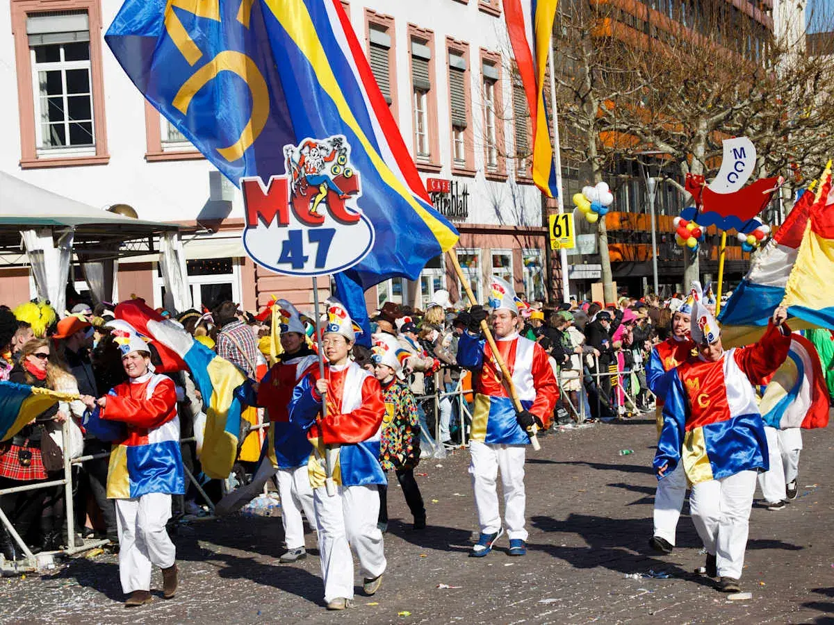 Bunte Kostüme und Fahnen beim Fasching 2026. Menschen feiern ausgelassen in der Stadt.
