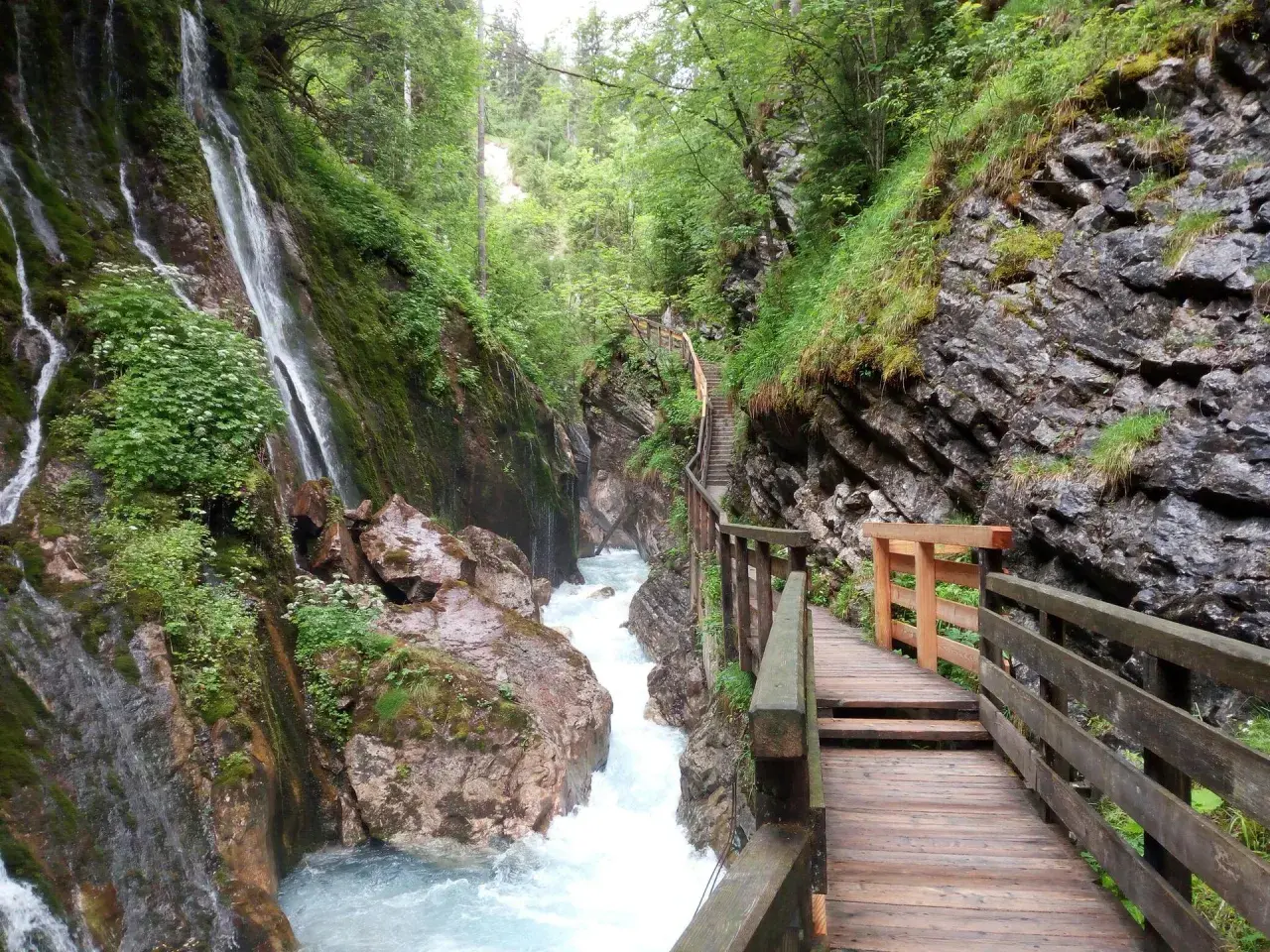Holzstege führen durch die Klamm Berchtesgaden, vorbei an tosendem Wasser und moosbewachsenen Felsen.