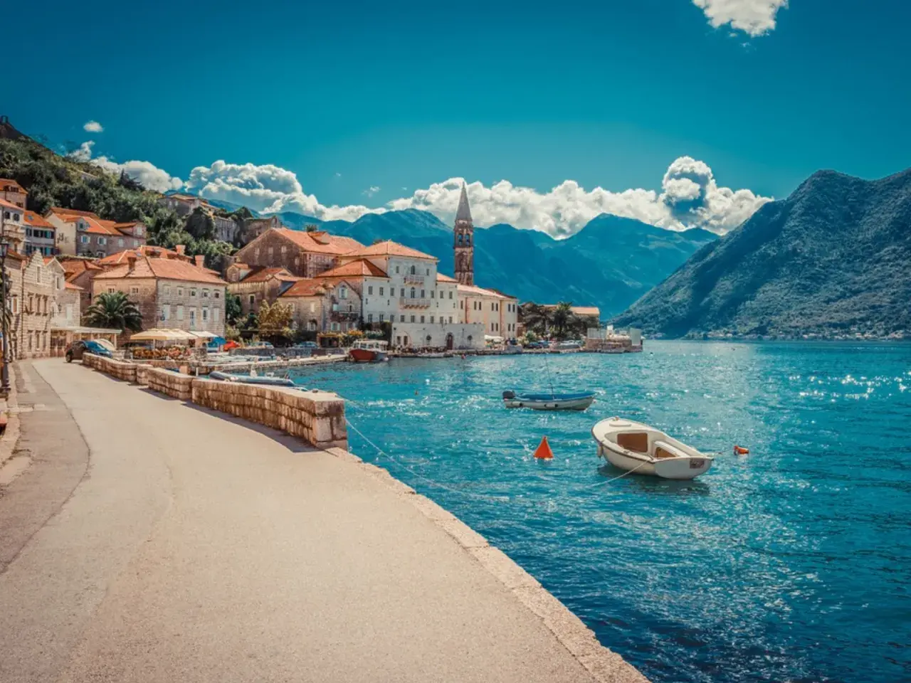 Blick auf eine malerische Küstenstadt mit roten Dächern und einem Kirchturm, umgeben von Bergen. Boote schaukeln auf dem türkisfarbenen Wasser. Ein Traumziel!