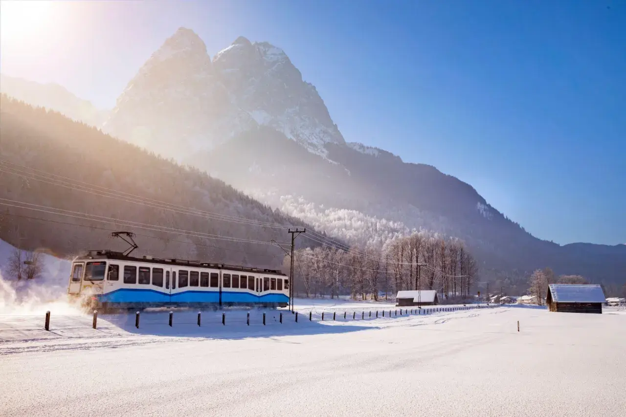 Blauer Zug fährt durch verschneite Alpenlandschaft, tolle Winterurlaub Ideen für Ihre Reise.