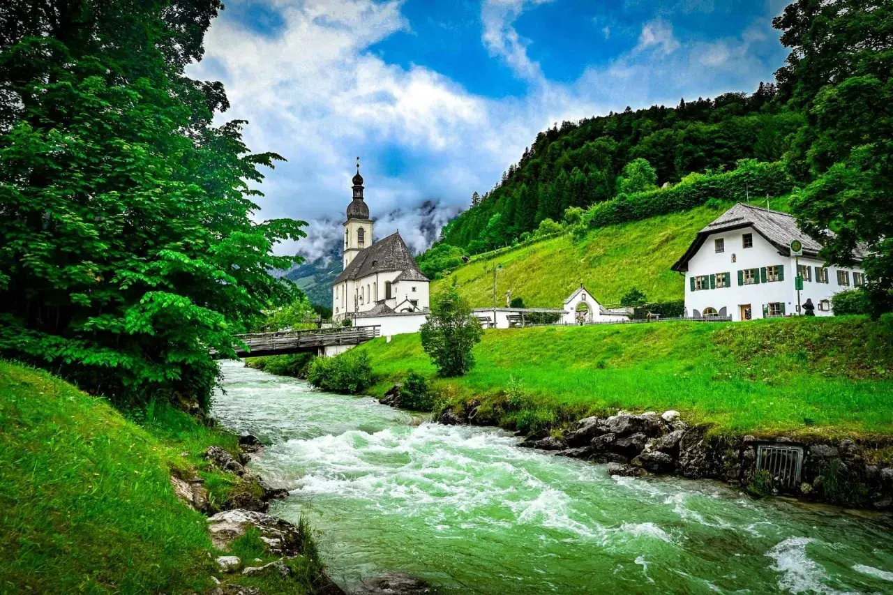 Grüner Fluss fließt an Kirche und Haus vorbei. Hier kann man in Berchtesgaden die Natur genießen und die Seele baumeln lassen.