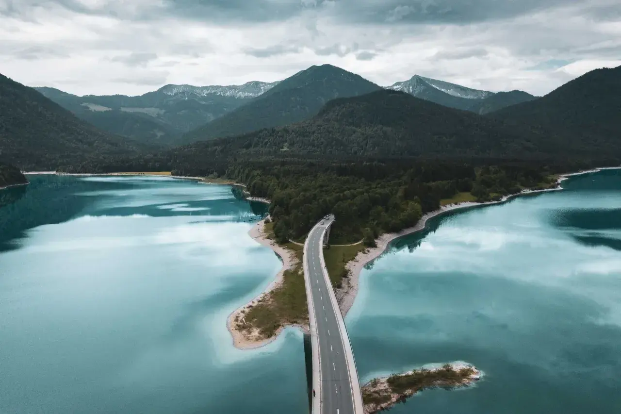 Brücke über türkisfarbenen See, umgeben von bewaldeten Bergen. Ein malerischer Ort für besondere Ausflugsziele.