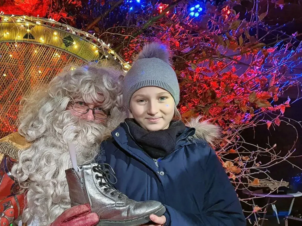 Ein Mädchen mit Mütze und Weihnachtsmann auf dem Weihnachtsmarkt Sassnitz. Er hält einen silbernen Stiefel.