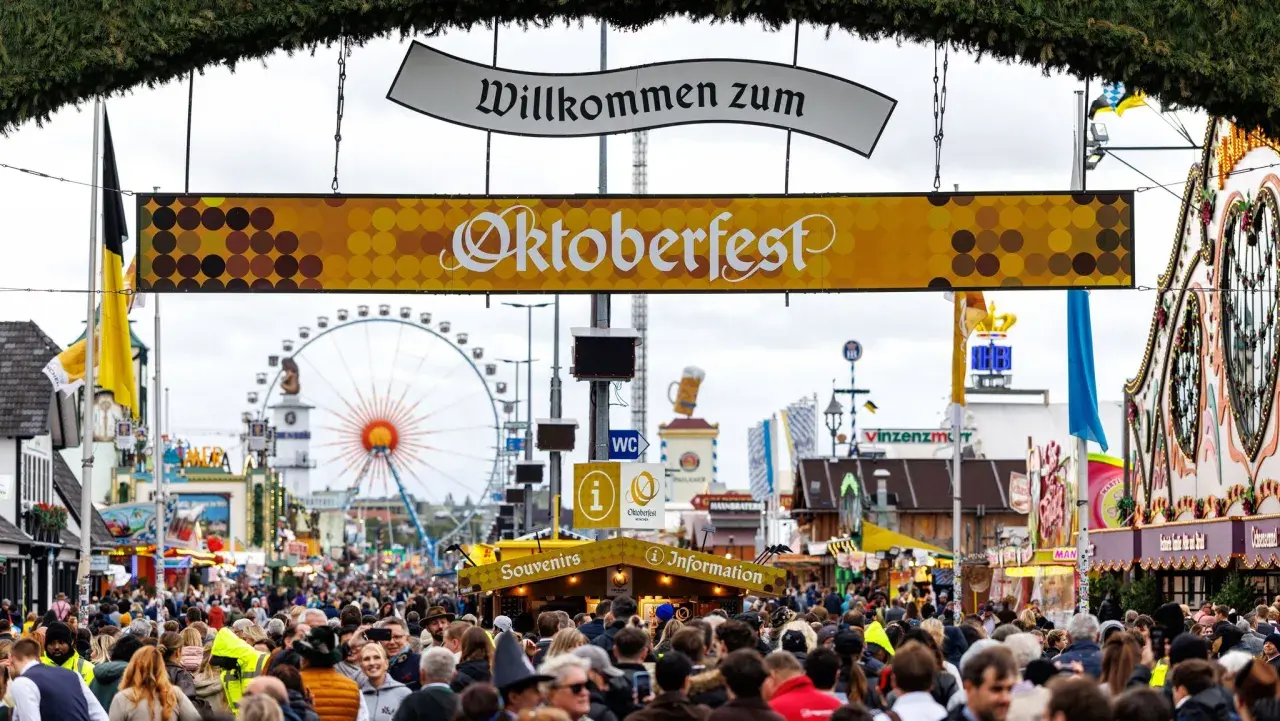 Volle Gassen beim Oktoberfest. Ein Schild verkündet "Willkommen zum Oktoberfest". Eintritt kostet das Oktoberfest nicht, aber die Attraktionen und das Bier.