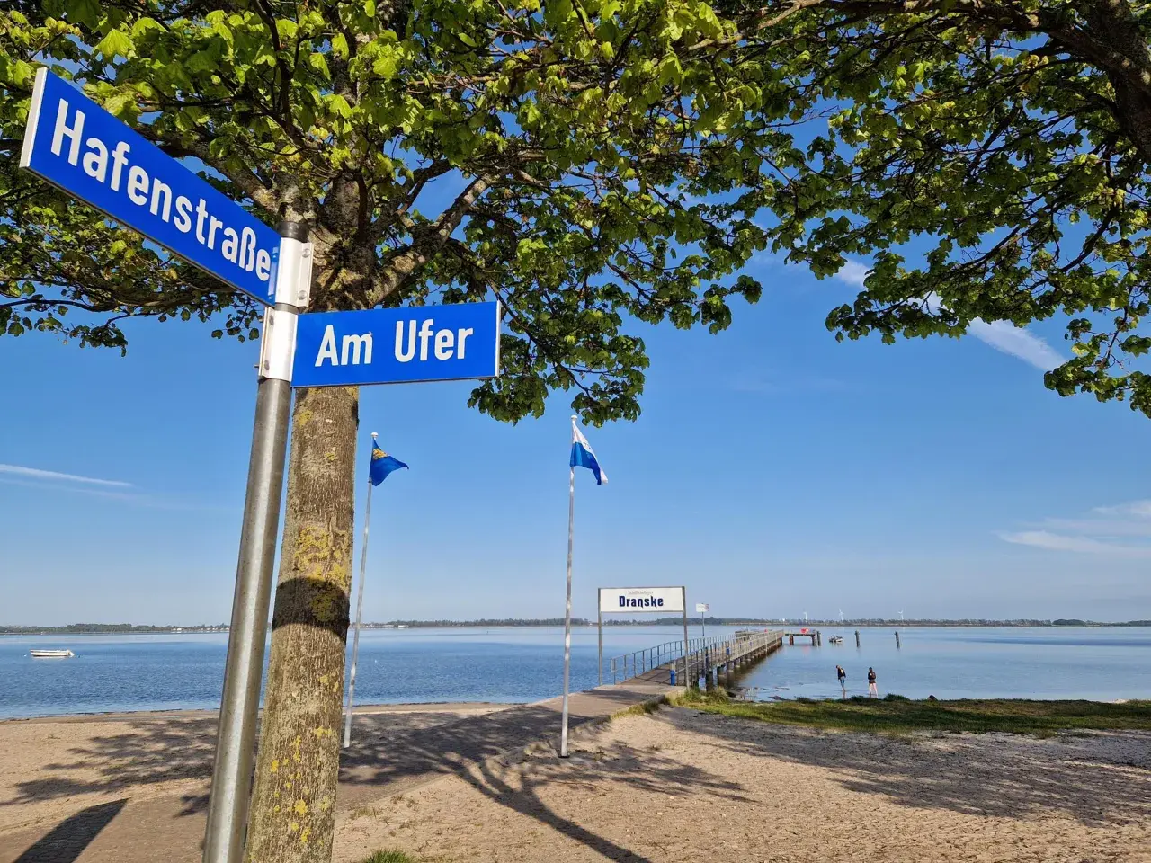 Schilder "Hafenstraße" und "Am Ufer" weisen den Weg zur **dranske strandpromenade**. Ein Steg führt ins ruhige Wasser.