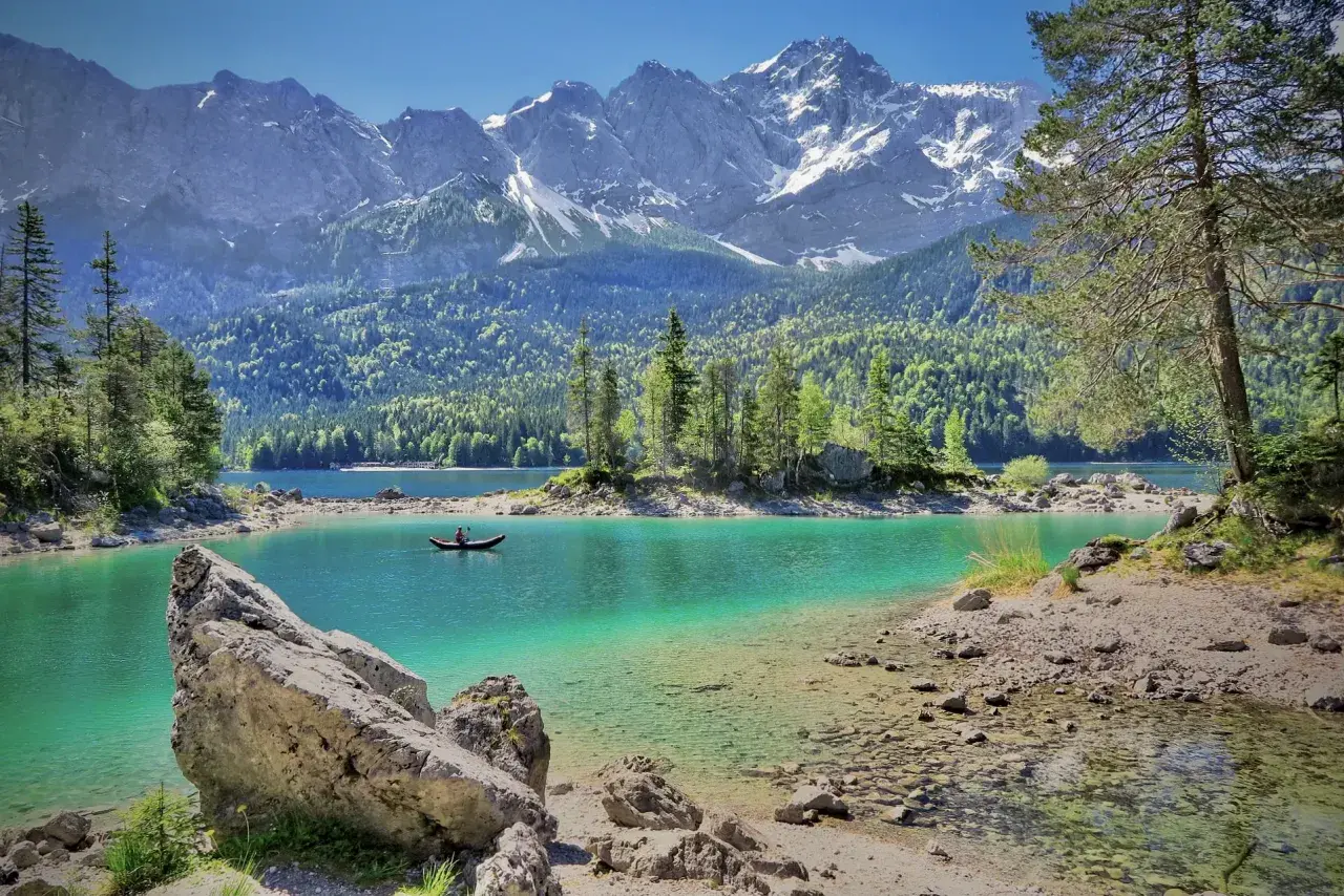 Türkiser Bergsee in Deutschland mit schneebedeckten Gipfeln im Hintergrund. Ein Kanufahrer genießt die Ruhe.