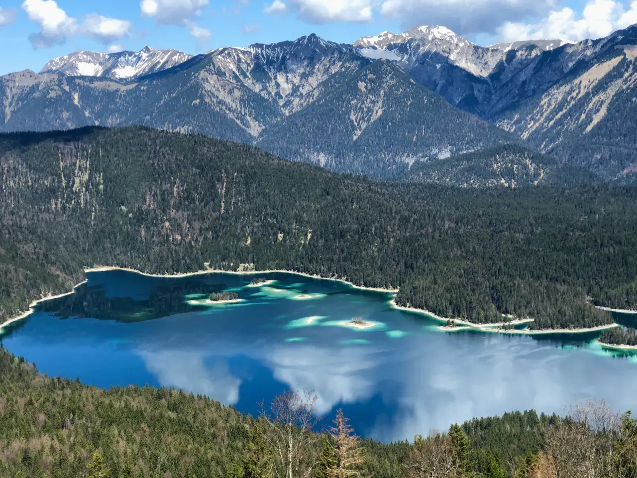 Blick vom Eibsee zur Zugspitze: Türkisblaue Wasserflächen, bewaldete Hänge und schneebedeckte Gipfel. Ein Traumziel für Wanderer.