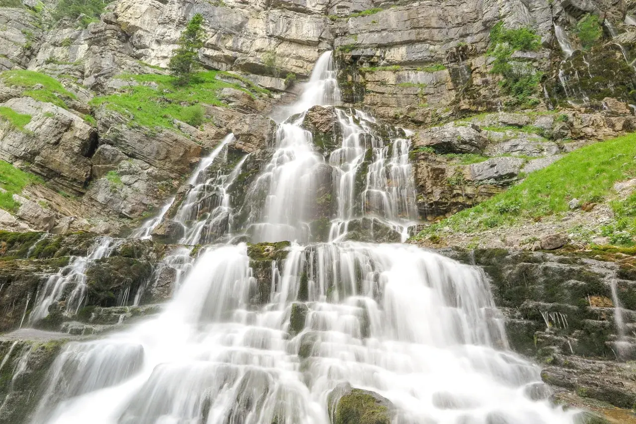 Ein beeindruckender, mehrstufiger murnau wasserfall stürzt über moosbewachsene Felsen in die Tiefe, umgeben von steilen, grünen Hängen.