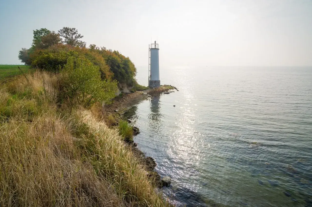 Leuchtturm auf der Halbinsel Zudar, umgeben von üppiger Vegetation und dem glitzernden Meer.