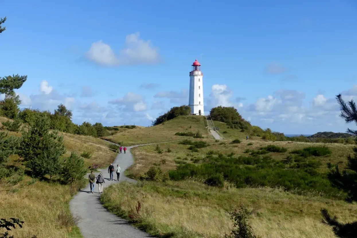 Ein Hiddensee Tagesausflug führt über grasbewachsene Hügel zum Leuchtturm. Wanderer genießen die sonnige Aussicht.