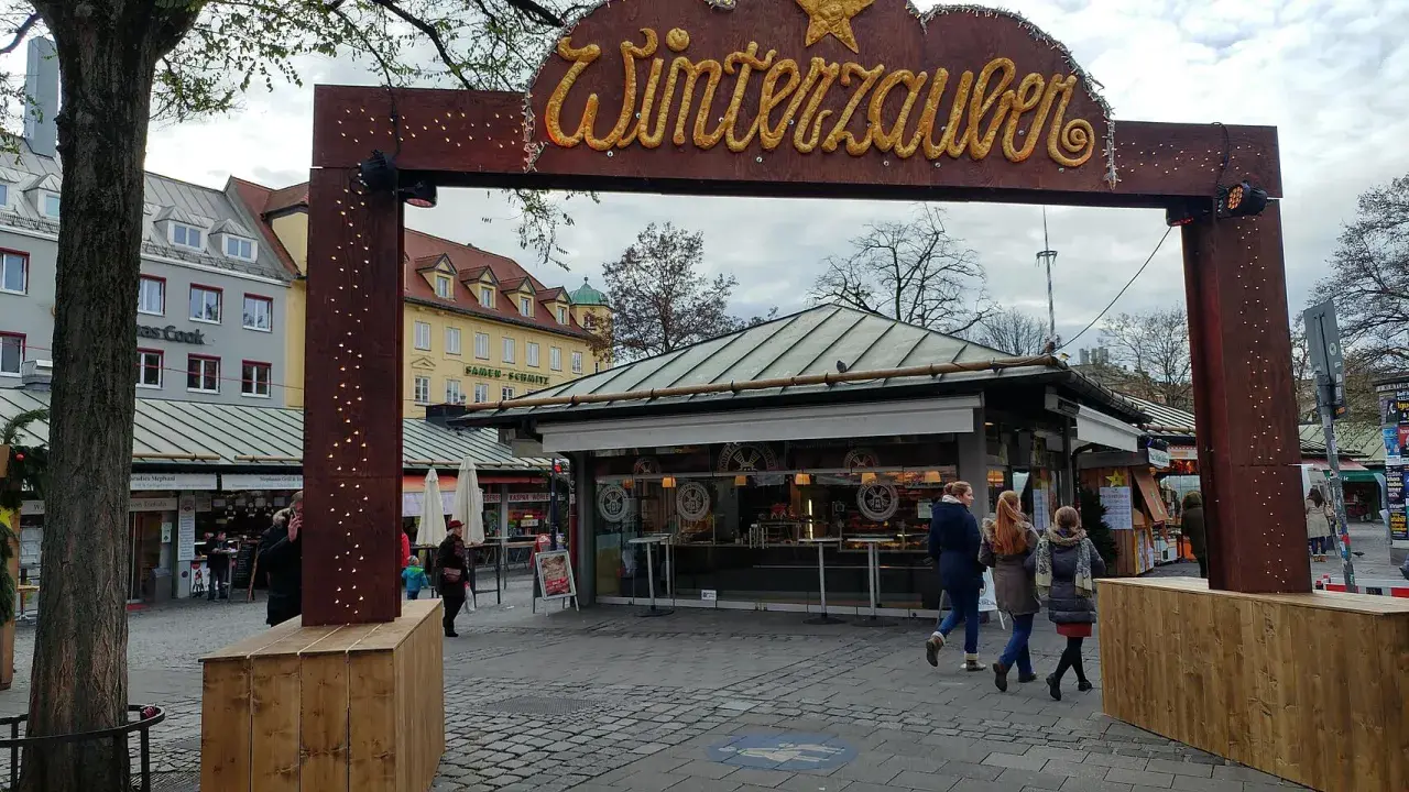 Der Viktualienmarkt zeigt seinen Winterzauber. Menschen schlendern vorbei an Ständen, die auf den Weihnachtsmarkt einstimmen.