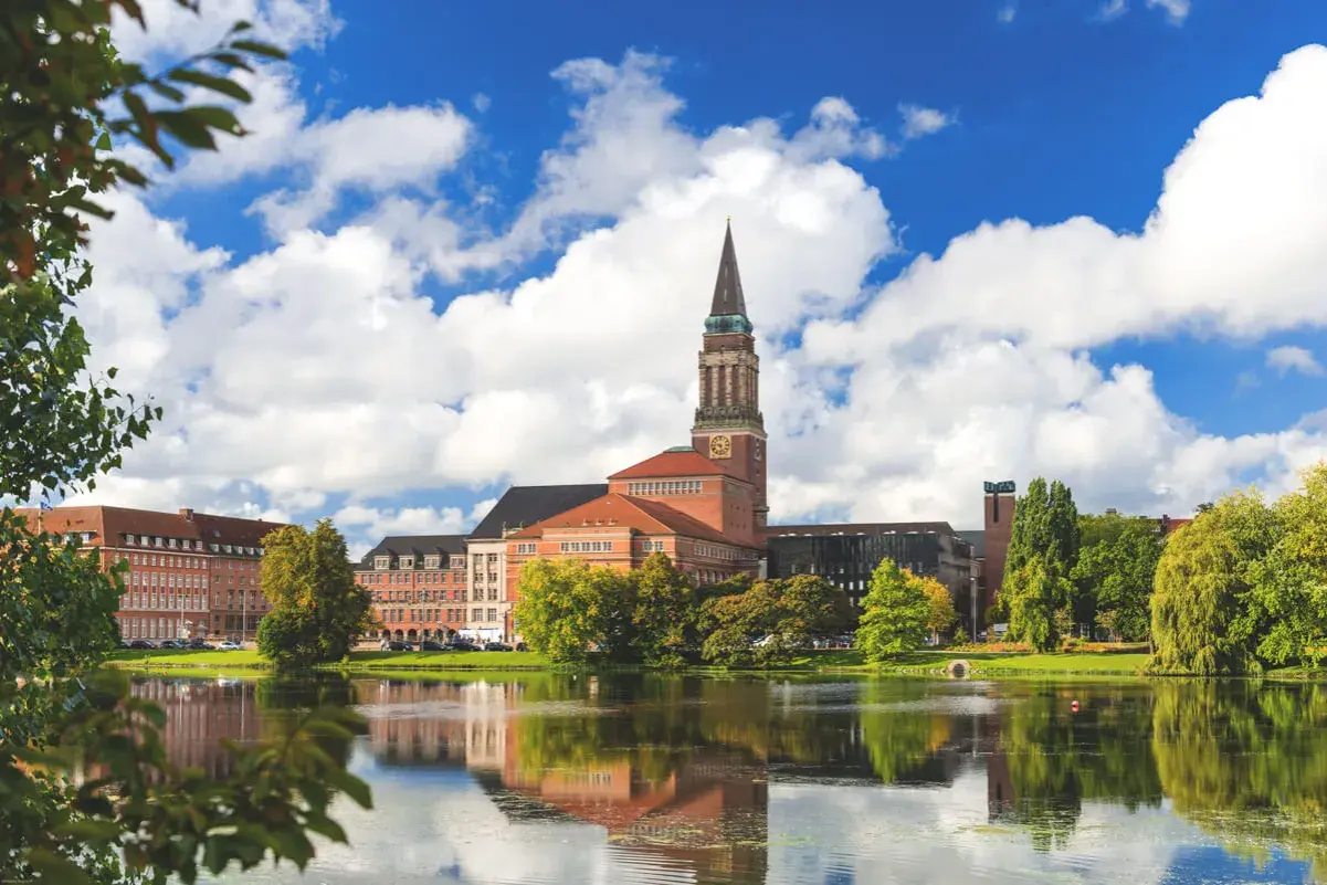 Ein malerischer Blick auf das Rathaus von Kiel, perfekt für Kiel Sightseeing. Der Turm ragt in den blauen Himmel, während sich das Gebäude im ruhigen Wasser spiegelt.