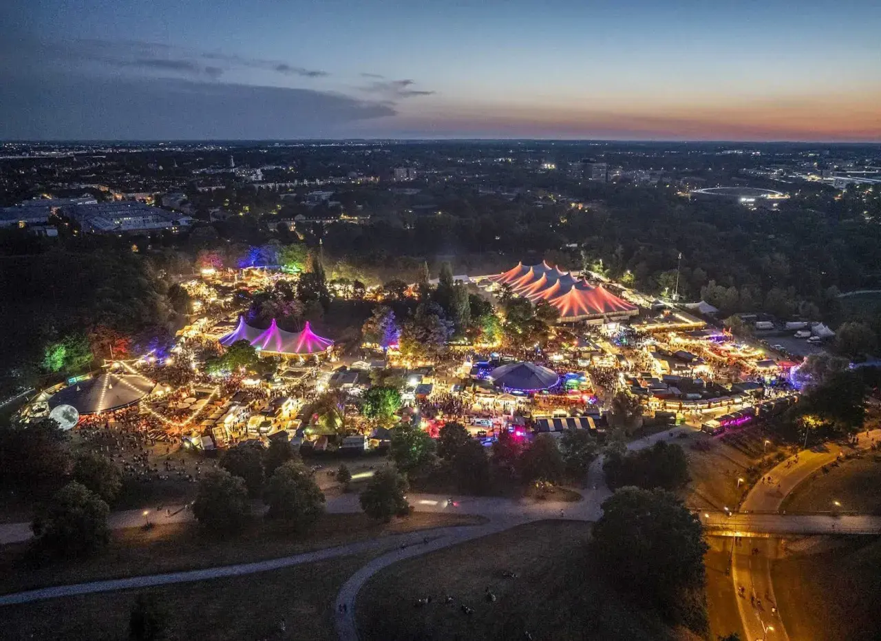 Nachtansicht des beleuchteten Tollwood Festivals im Olympiapark München mit bunten Zelten und Lichtern.