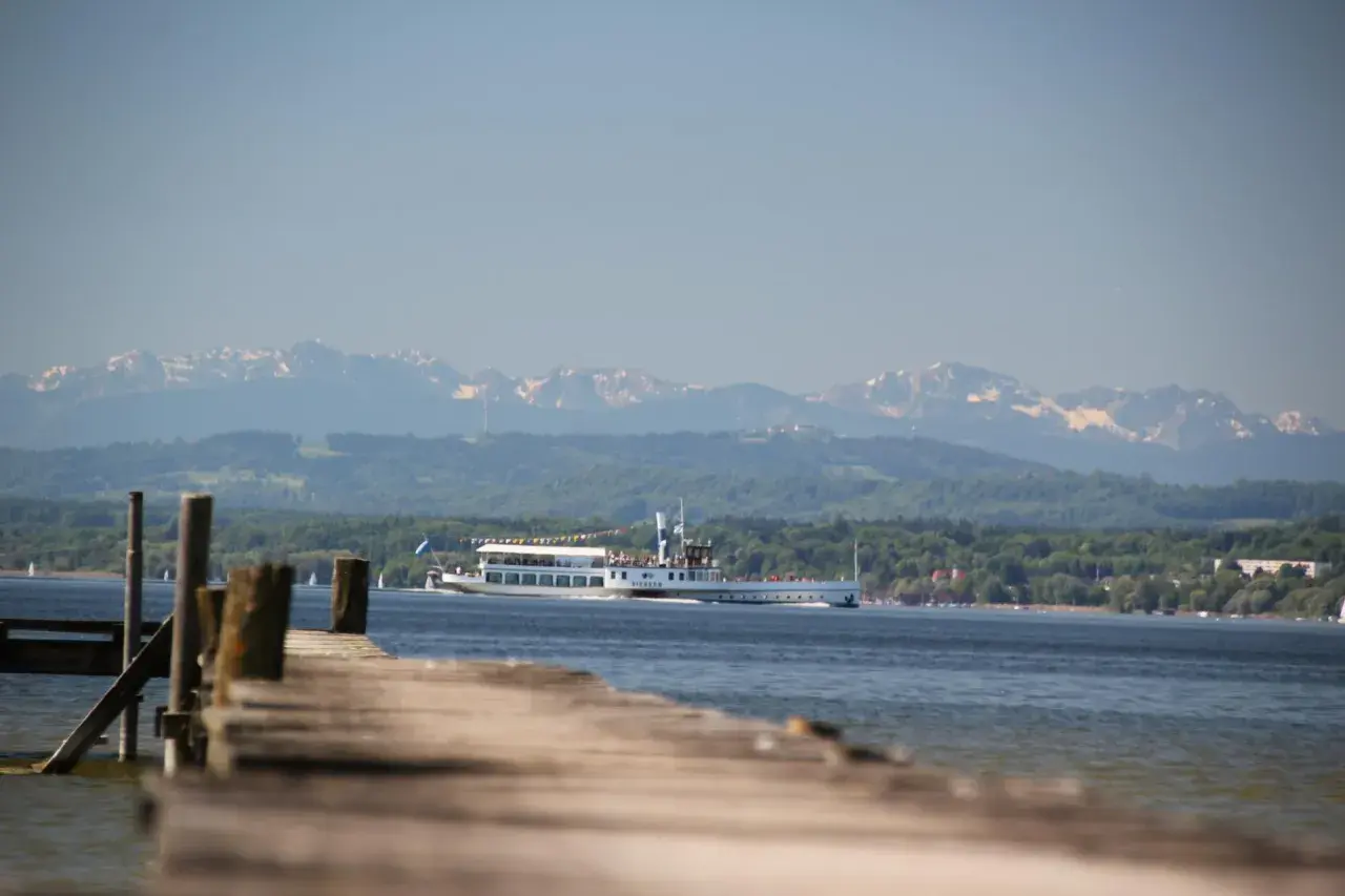 Holzsteg am Ammersee mit einem Ausflugsschiff, im Hintergrund die schneebedeckten Ammersee Berge.