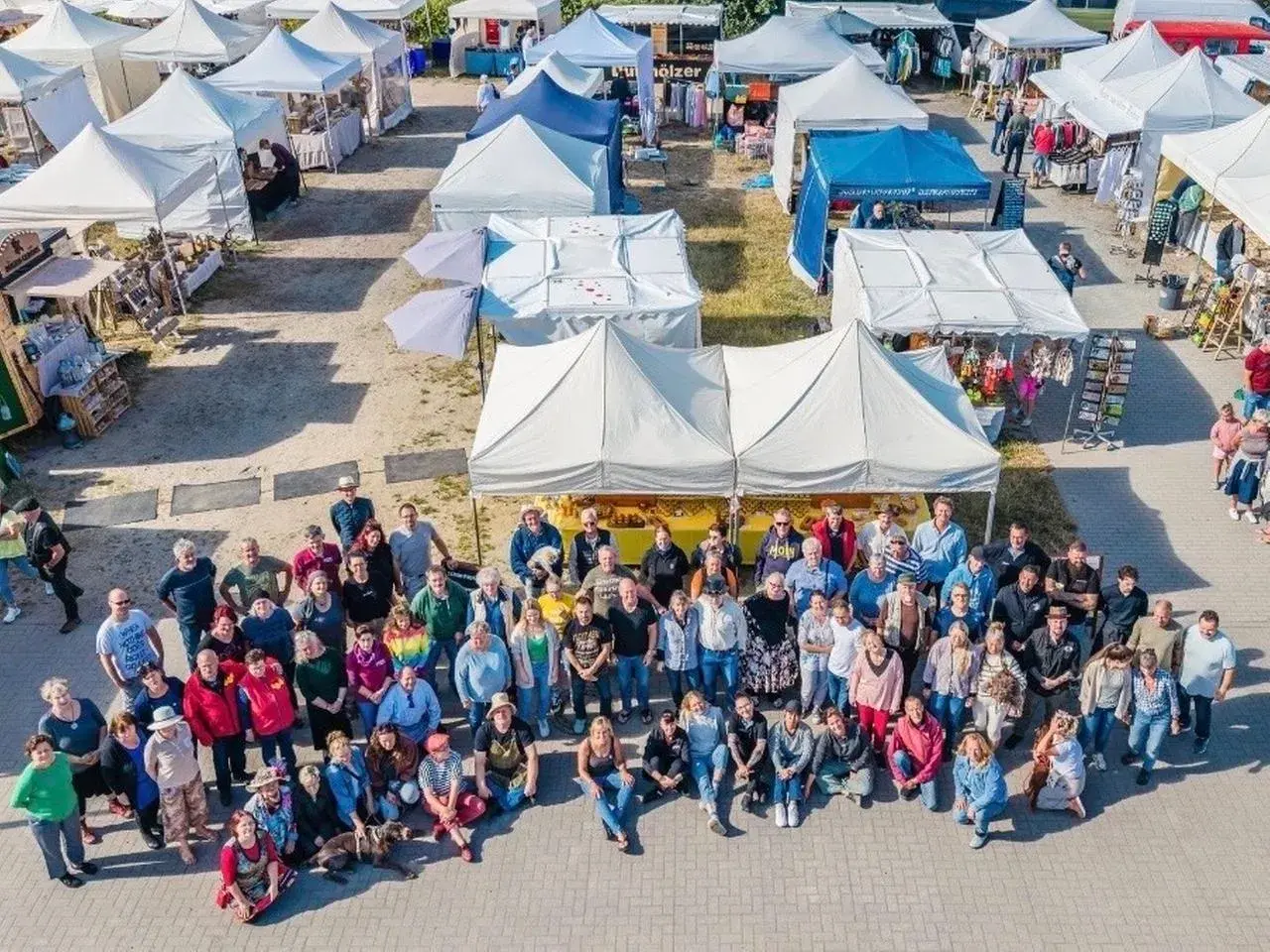 Große Gruppe feiert auf dem wochenmarkt thiessow. Viele Stände mit Waren und Zelten im Hintergrund.