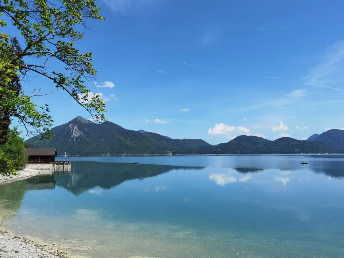 Karibik-Feeling am Walchensee: Ein Boot gleitet über das spiegelglatte Wasser, Berge im Hintergrund laden zum Baden ein.
