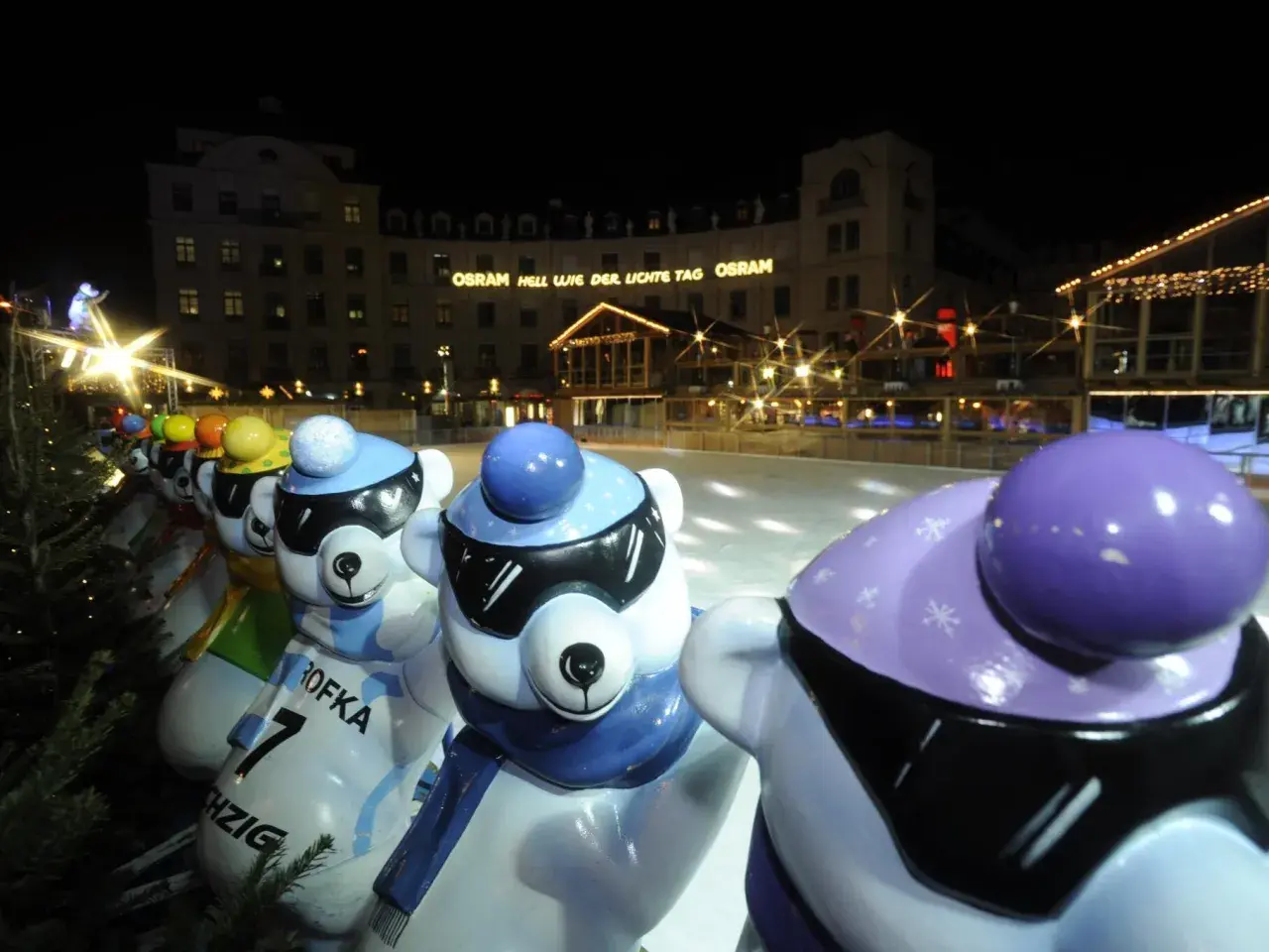 Bunte Eisbären-Figuren am Stachus Weihnachtsmarkt in München, mit Lichtern und einer Eisbahn im Hintergrund.