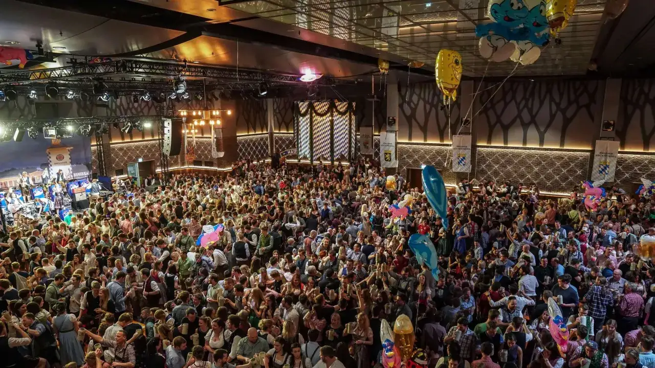Volles Festzelt beim Starkbierfest Nockherberg. Menschen in Tracht feiern ausgelassen, mit Bierkrügen in den Händen und bunten Ballons über ihnen.