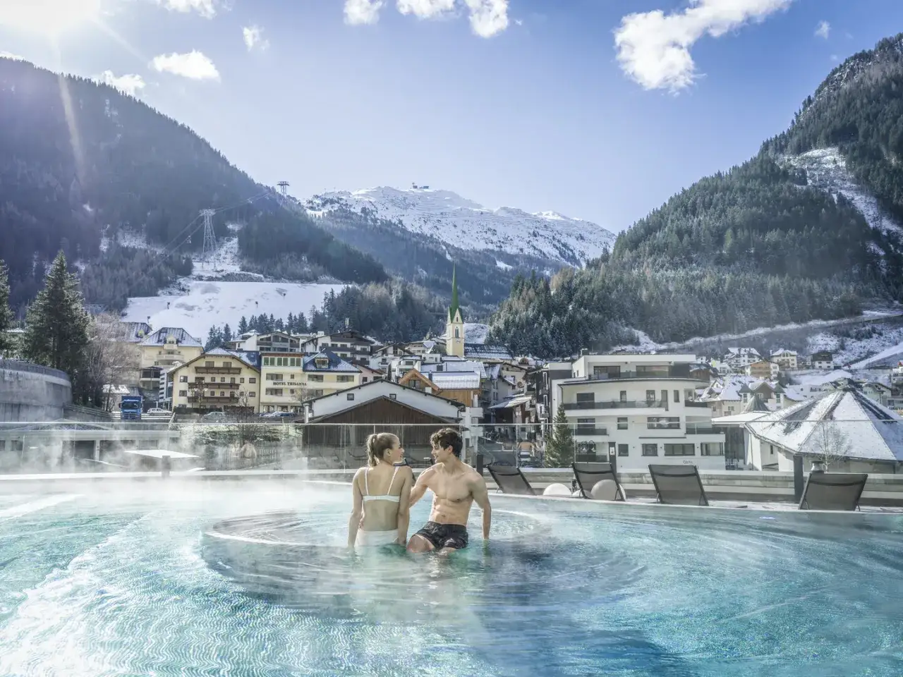 Ein Paar genießt den warmen Pool mit Blick auf ein verschneites Bergdorf. Perfekte winterurlaub ideen für Entspannung und Romantik.