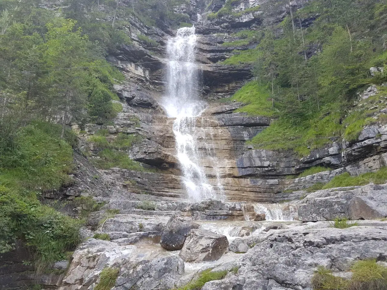 Ein tosender eibsee wasserfall st&uuml;rzt &uuml;ber Felsen in ein steiniges Bachbett. Gr&uuml;ne Vegetation umrahmt die Szenerie.