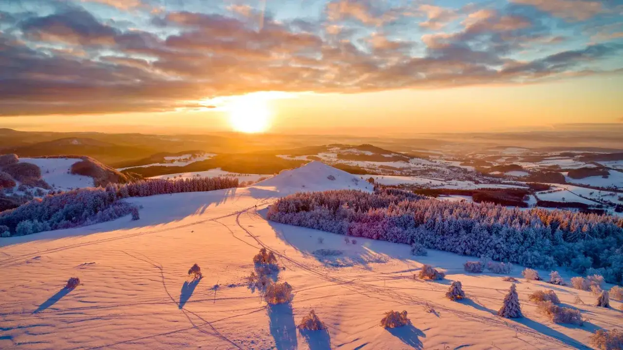 Sonnenuntergang über verschneiten Hügeln und Wäldern. Ein perfekter Ort für die besten Skigebiete, mit langen Schatten und goldenem Licht.