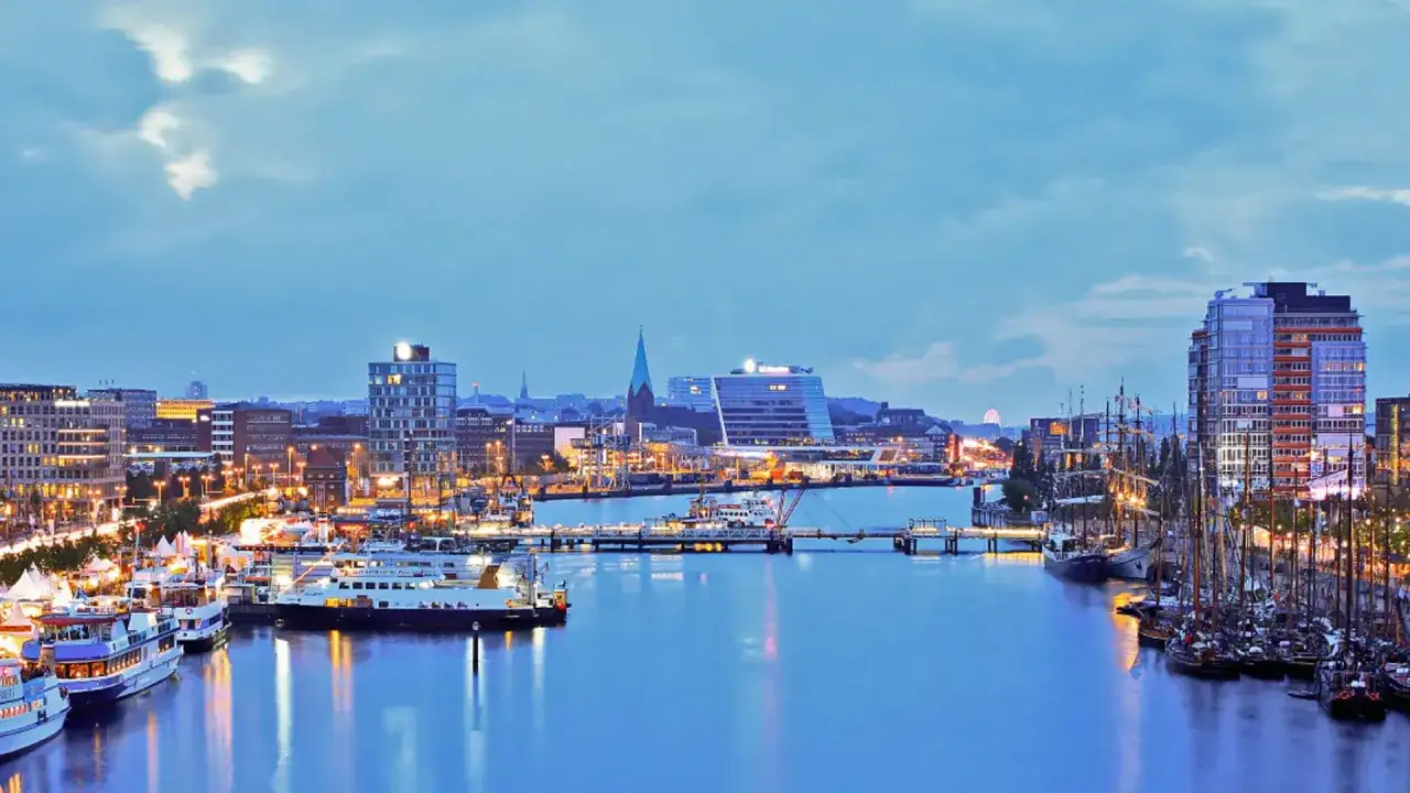Abendliche Hafenansicht von Kiel mit beleuchteten Gebäuden und Schiffen. Ein perfekter Ort für Kiel Sightseeing.