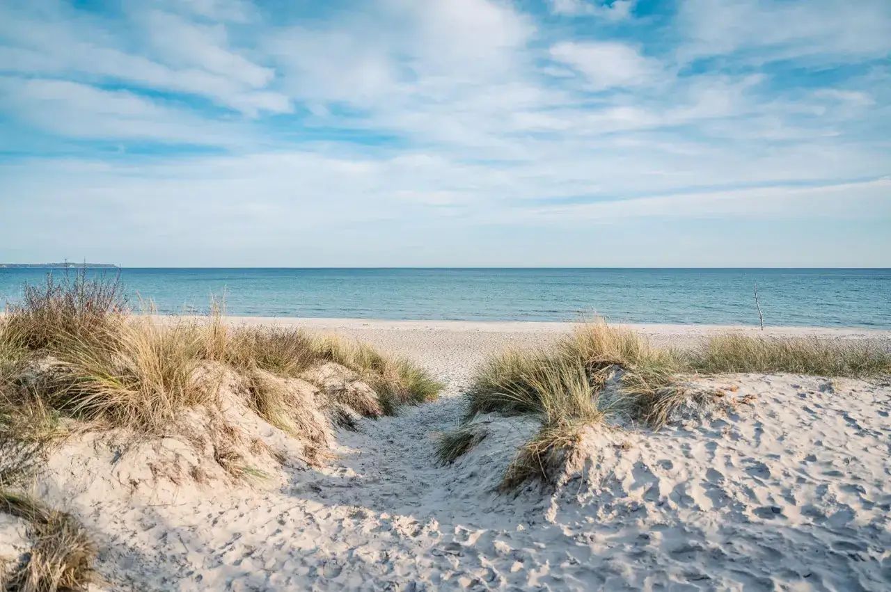 Ein Weg durch die Dünen führt zur Schaabe, wo das Meer und der Himmel in sanften Blau- und Weißtönen verschmelzen.