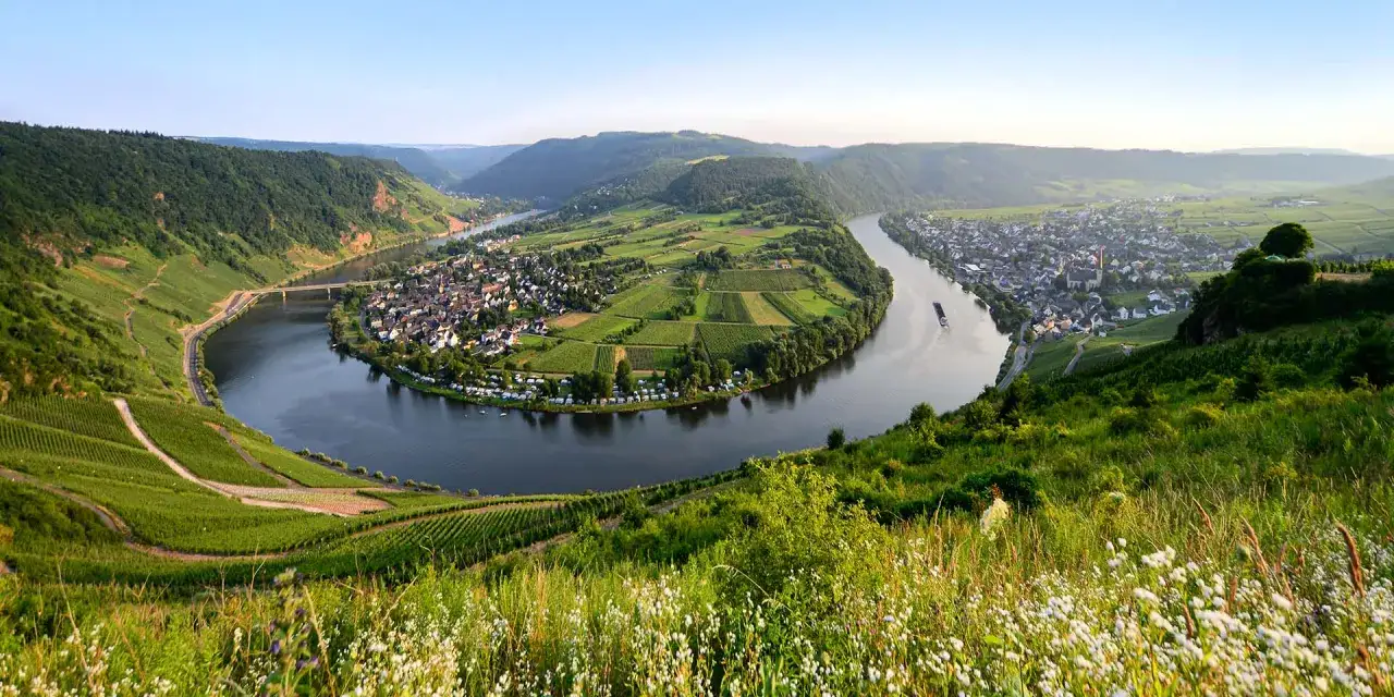 Ein malerischer Flusswindung mit Weinbergen, einem Dorf und grünen Hügeln. Perfekt für unbekannte Reiseziele.