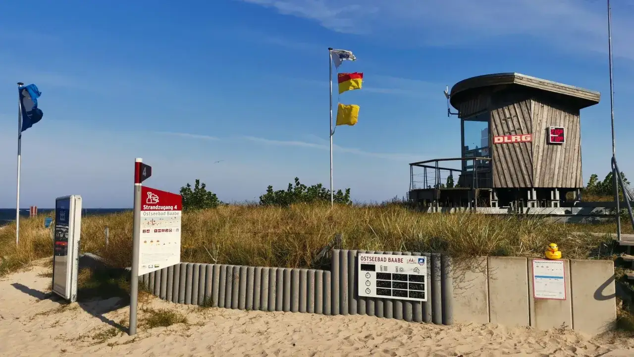 Strandzugang 4 im Ostseebad Baabe. Rettungsturm der DLRG, Flaggen und Informationstafeln am Strand.