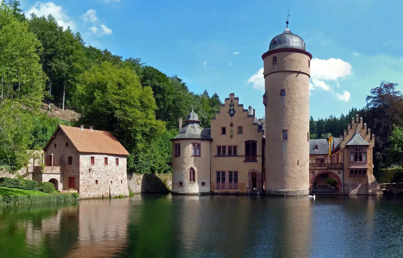 Wasserschloss inmitten grüner Wälder, ein malerisches Motiv für Ausflugsziele Spessart. Ein Turm und Nebengebäude spiegeln sich im Wasser.