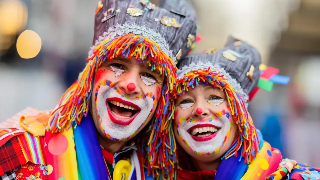 Zwei lachende Clowns mit bunten Perücken und Schminke, bereit für den Fasching 2027.