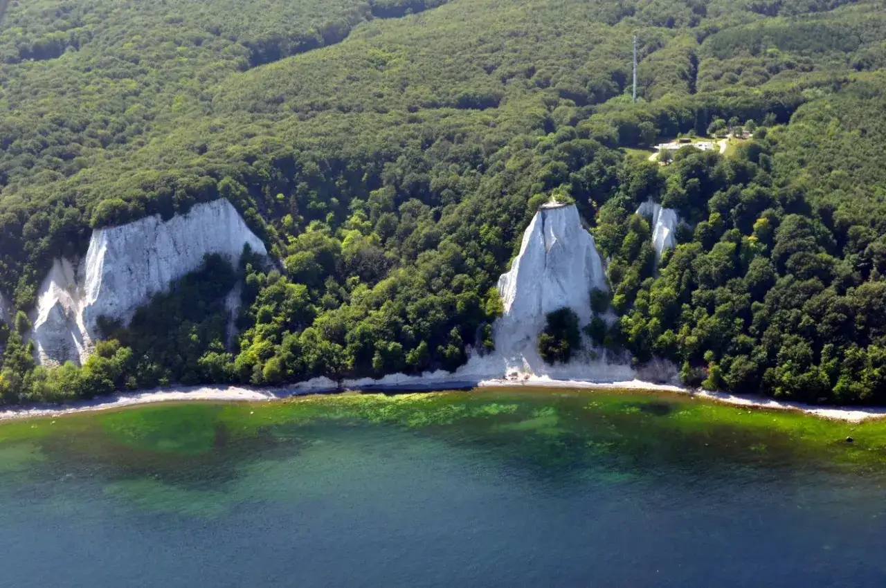 Weiße Kreidefelsen ragen aus dem grünen Wald auf der Halbinsel Jasmund empor, umspült von klarem, türkisfarbenem Wasser.