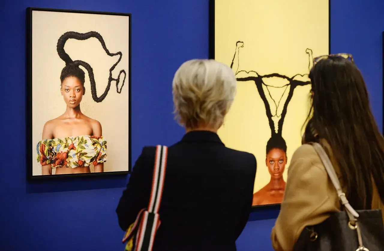 Besucher betrachten Kunstwerke bei der ausstellung hypo kunsthalle. Ein Bild zeigt eine Frau mit afrikanisch geformten Haaren, das andere eine Frau mit Gebärmutter-Frisur.