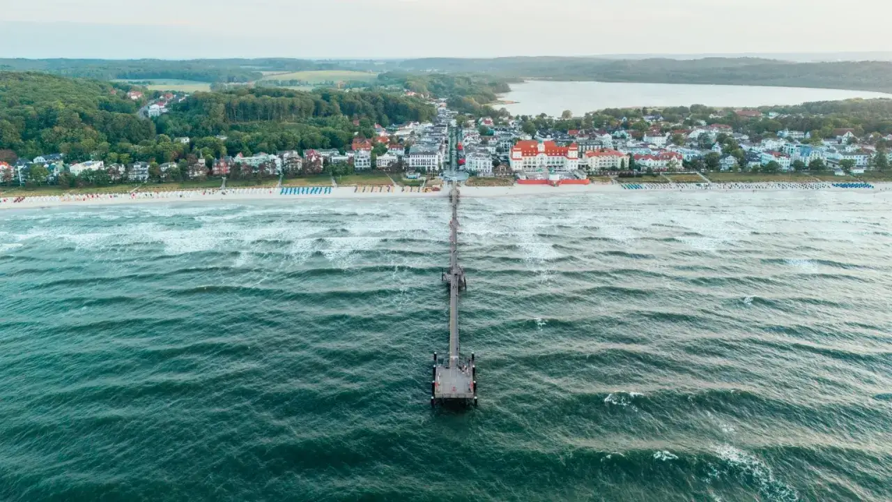 Die Seebrücke Binz erstreckt sich ins Meer, mit dem Strand und der Kurkarte Binz im Hintergrund.