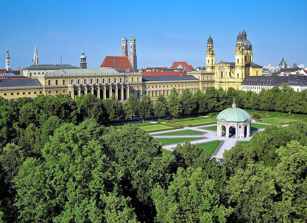 Blick &uuml;ber gr&uuml;ne B&auml;ume auf den Odeonsplatz M&uuml;nchen mit der Theatinerkirche und dem Hofgarten.