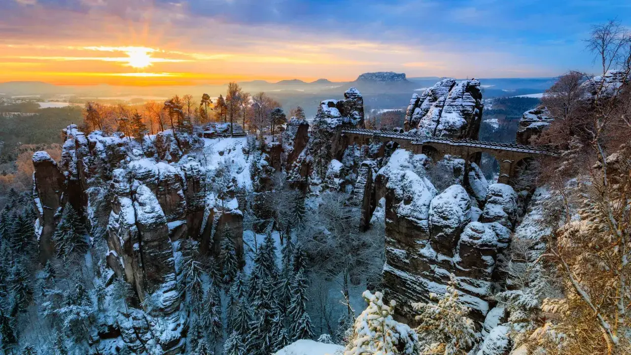 Winterliche Felsformationen mit Schnee bedeckt, die Basteibr&uuml;cke &uuml;berspannt die Schlucht. Ein malerisches Motiv f&uuml;r Ausflugsziele Sachsen bei Sonnenuntergang.