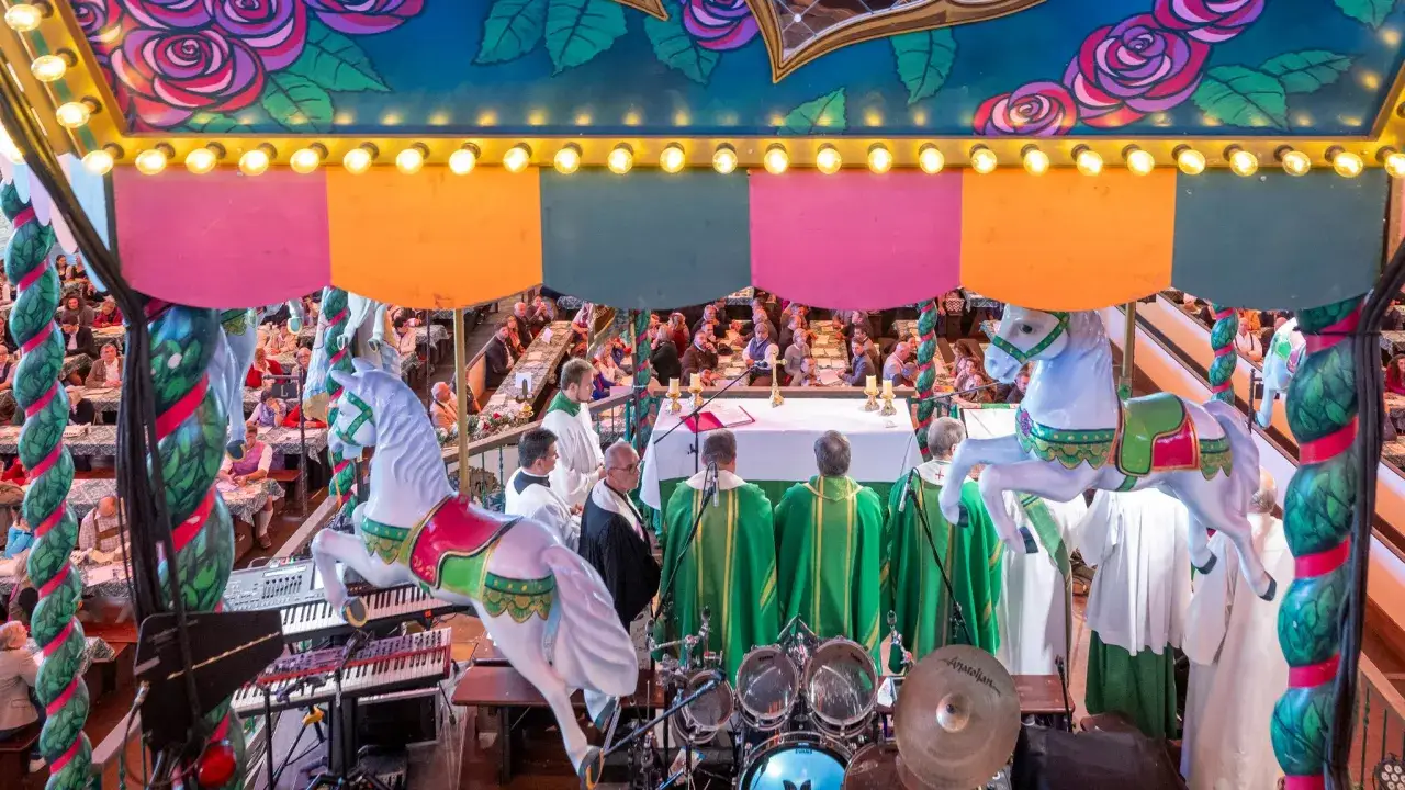 Festliche Messe auf dem Oktoberfest, mit Geistlichen in grünen Gewändern und einer Kapelle. Ein ungewöhnlicher Ort für