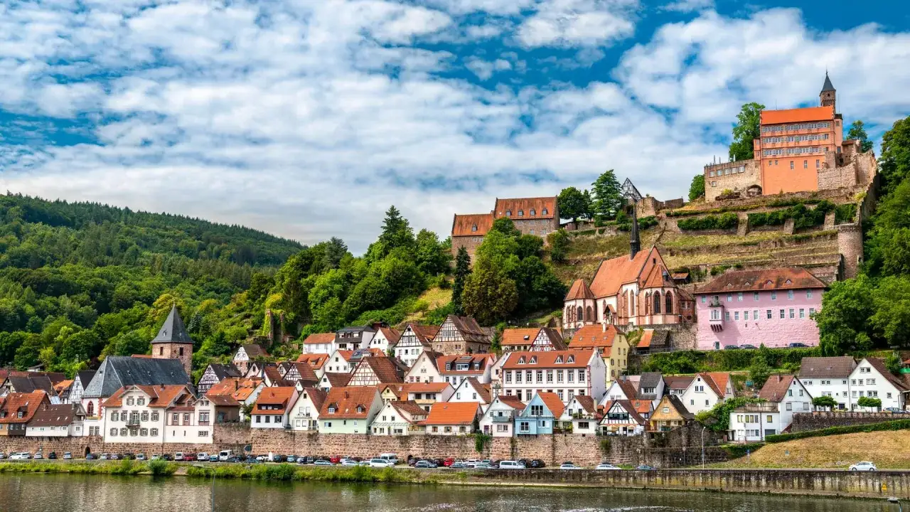 Muttertag unternehmung: malerisches Dorf mit Burgruine und Kirche am Flussufer, umgeben von grünen Hügeln.