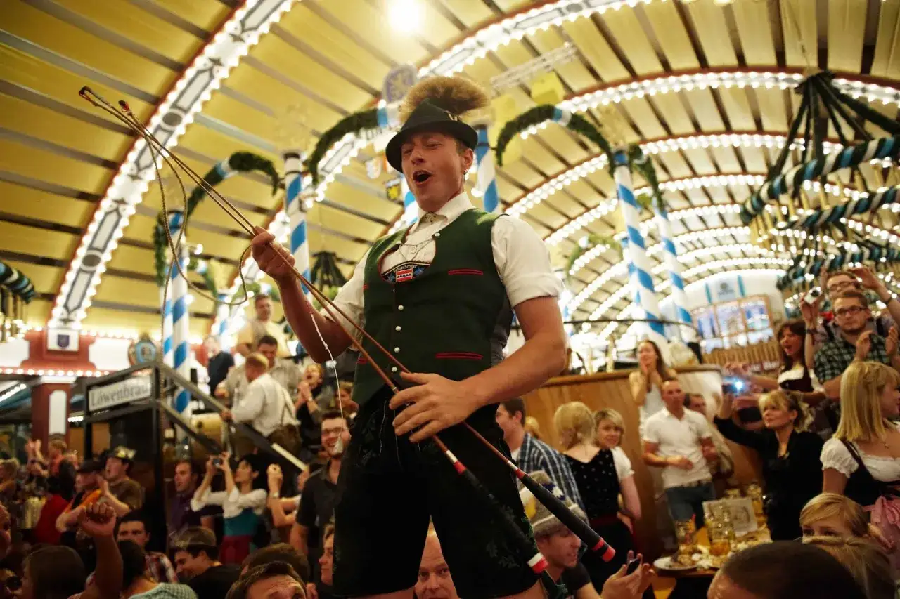 Ein Mann in Tracht hält Peitschen und macht Lärm. So macht man auf dem Oktoberfest Stimmung!