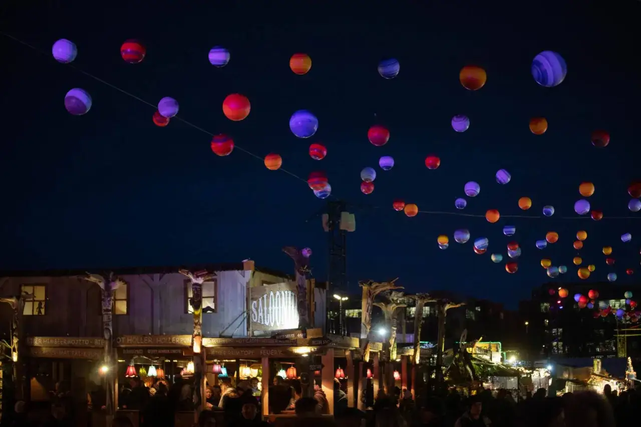 Bunte Lichterketten über dem weihnachtsmarkt theresienwiese. Menschen genießen die festliche Atmosphäre unter dem Sternenhimmel.