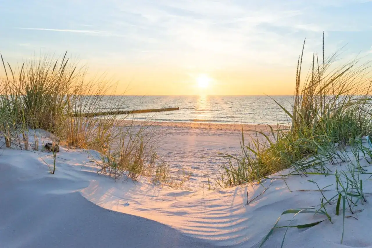 Sonnenuntergang am Juliusruh Strand. Dünen mit Gräsern säumen den Sand, die Ostsee glitzert im warmen Licht.