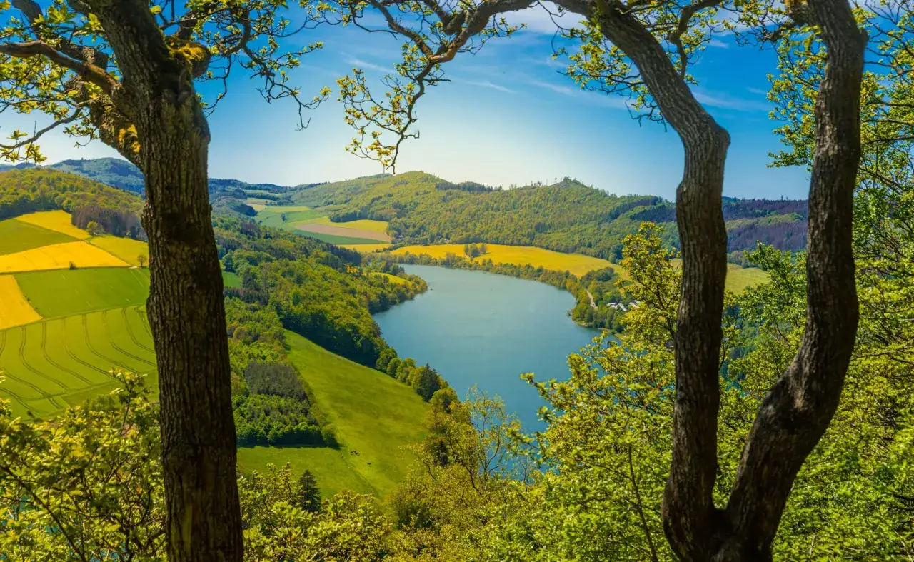 Ein idyllischer See umgeben von grünen Hügeln und gelben Feldern – perfekt, um sonntags unternehmen zu gehen und die Natur zu genießen.