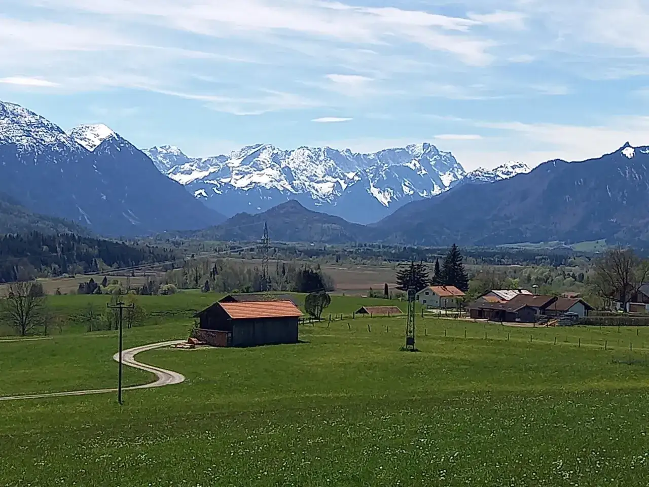 Idyllische Landschaft bei Murnau am Staffelsee mit schneebedeckten Bergen im Hintergrund, gr&uuml;nen Wiesen und einem Bauernhaus.