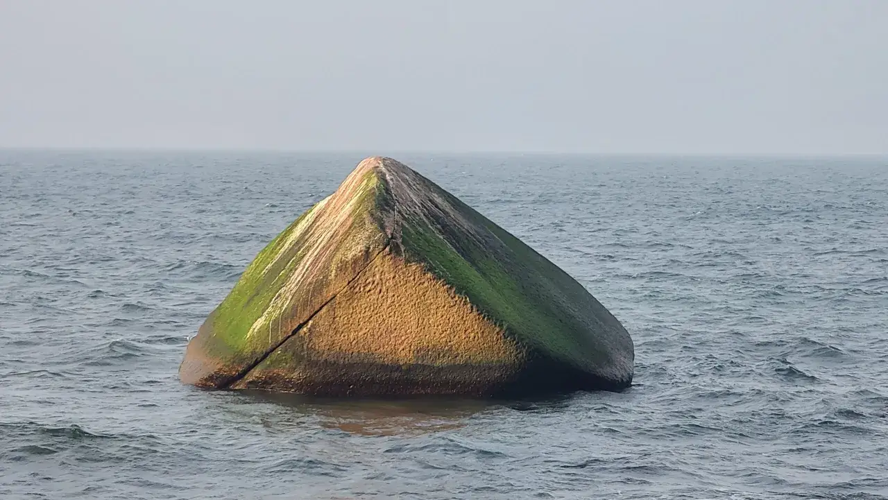 Ein moosbewachsener Felsen ragt aus dem Meer, ein einsamer Wächter am Lohme Strand.