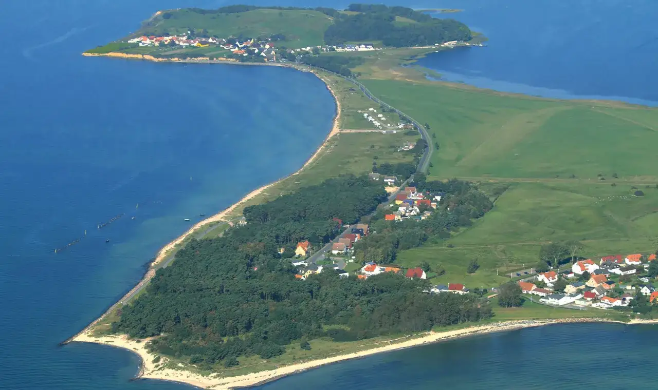 Luftaufnahme vom Thiessow Strand mit Häusern, Wald und Feldern, die sich an der Küste entlangschlängeln.