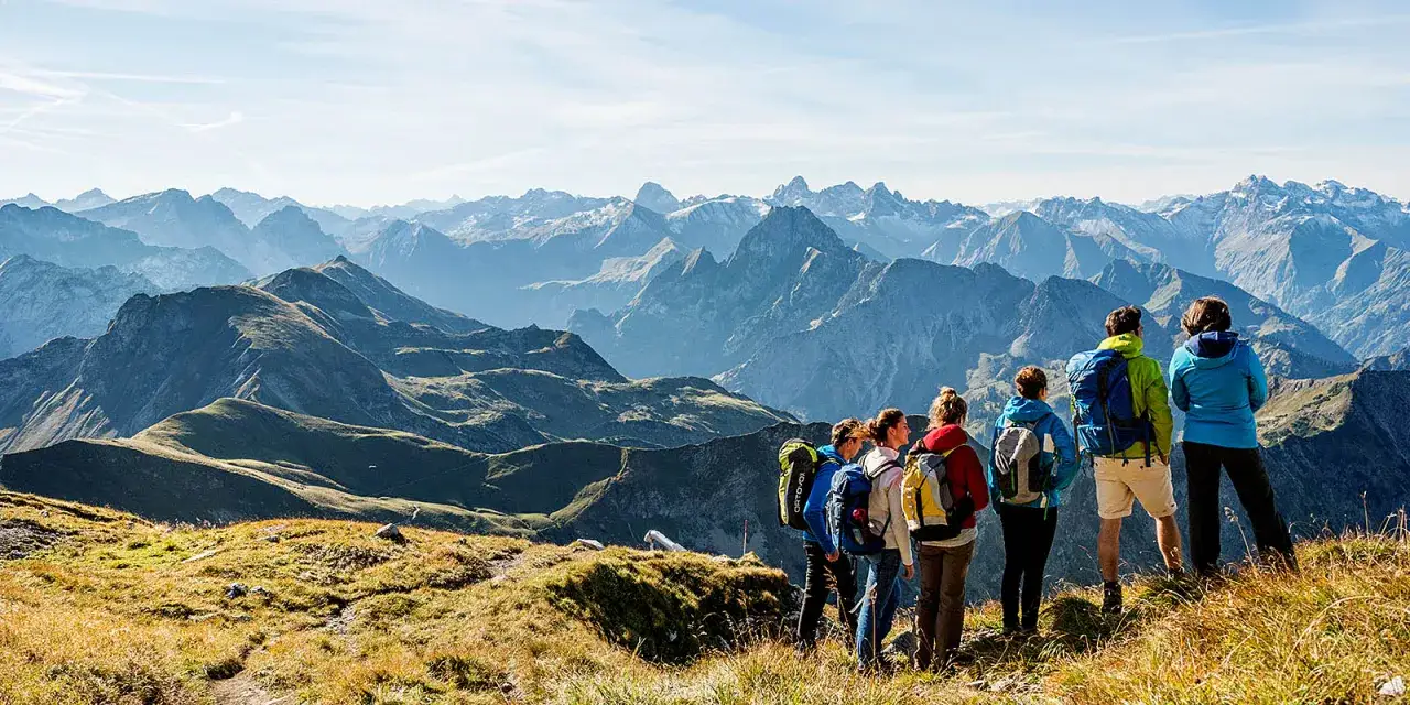 Gruppe von Wanderern genießt die atemberaubende Aussicht auf die Alpen. Sie stehen auf einem grasbewachsenen Hang und blicken auf eine majestätische Bergkette.